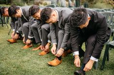 a group of men in suits and ties tying their shoes on a bench at a wedding