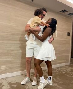 a man and woman in white clothes holding a baby while standing next to each other