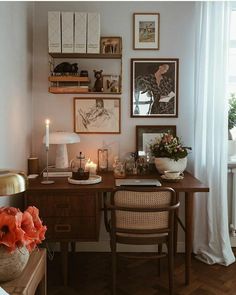 a desk with flowers and candles on it in front of pictures hanging on the wall