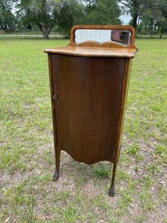 an old wooden cabinet sitting in the middle of a field with grass and trees behind it