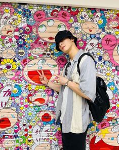 a young man standing in front of a wall covered with cartoon character drawings and holding a backpack