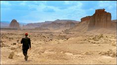 a man walking through the desert with mountains in the background