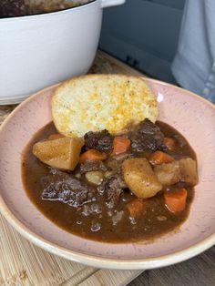 a bowl filled with stew and bread on top of a wooden table