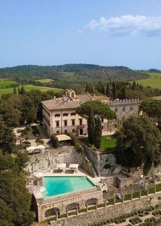 an aerial view of a large house with a pool in the foreground and trees surrounding it