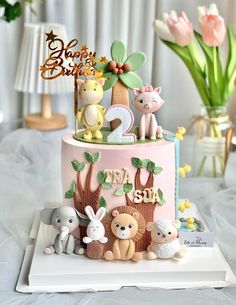 a pink cake with animals and trees on top is sitting on a white tablecloth