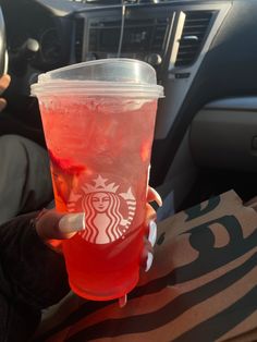 a person holding up a cup of drink in their hand with ice and strawberries on it