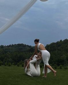 two women in white dresses are playing with a frisbee on the grass outside