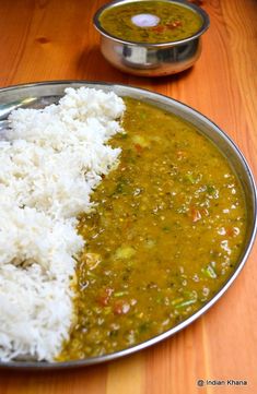 a metal plate topped with rice and green curry next to a silver bowl filled with white rice