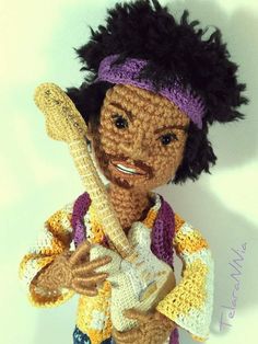 a crocheted doll holding a guitar and wearing a purple headband is smiling at the camera