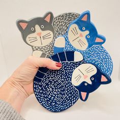 a hand is holding three plates with cats on them, one blue and the other grey