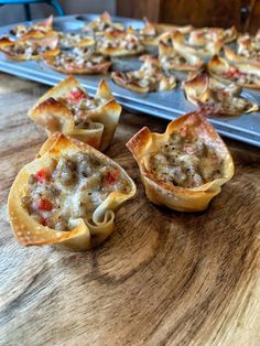 several mini pizzas with meat and cheese in them sitting on a table next to a baking sheet