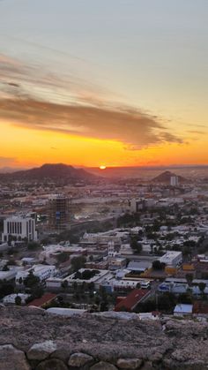 the sun is setting over a city with mountains in the background and clouds in the sky