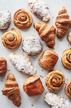 many different types of pastries on a white counter top with croissants and powdered sugar