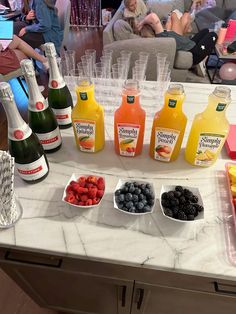 bottles of juice and fruit on a table with people in the background