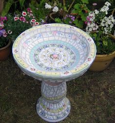 a decorative bird bath sitting on the ground next to potted plants and flowers in pots