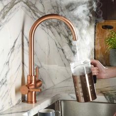 a woman is washing dishes in the kitchen with copper faucet and marble countertops