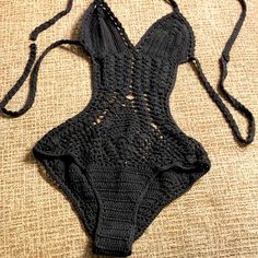 a crocheted black bikinisuit laying on top of a brown cloth covered floor