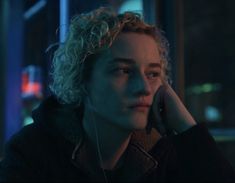 a young man with curly hair is talking on his cell phone while looking at the camera