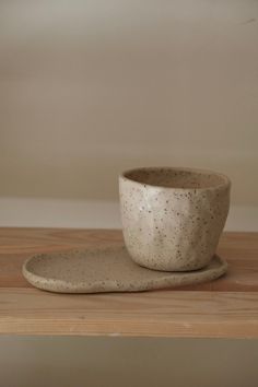 a white cup and saucer sitting on top of a wooden table next to a wall