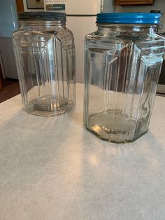 two glass jars sitting on top of a counter next to each other, one with a blue lid