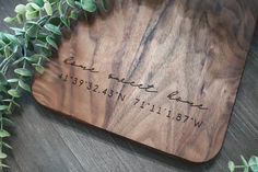 a wooden cutting board with writing on it next to some green plants and leaves in the background