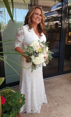 a woman standing in front of a glass door holding a bouquet of white and green flowers