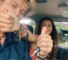 two people sitting in the back seat of a car, one pointing at the camera