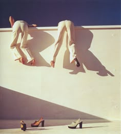 two people standing on the side of a wall with their feet in the air and one person wearing high heels