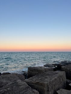 the sun is setting over the ocean and rocks