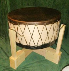 a large wooden drum sitting on top of a green cloth covered floor next to two small wooden stands