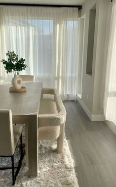 a dining room table and chairs in front of a window with white drapes on the windowsill