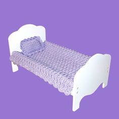 a small white bed with purple bedspread and pillows on it's sides