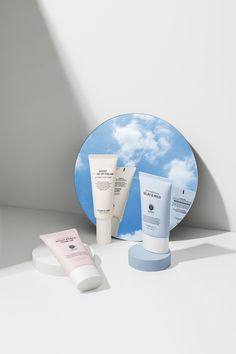 an assortment of skin care products sitting on a counter next to a mirror with clouds in the background