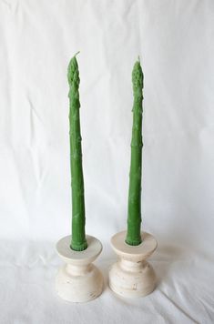 two green candles sitting on top of each other in small white vases with stems sticking out of them