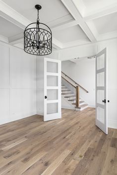 an empty living room with white walls and wood flooring, chandelier hanging from the ceiling