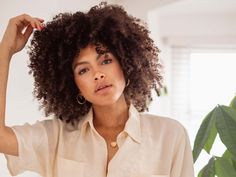 a woman with curly hair is holding her hand on her head and looking off to the side