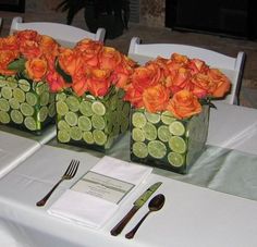 two vases filled with orange flowers sitting on top of a table next to silverware