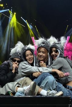 four people sitting on top of a stage with lights behind them and one person holding a cell phone