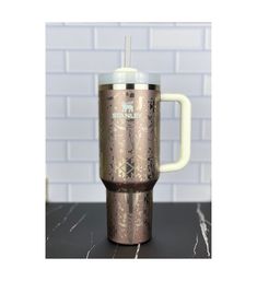 a metallic travel mug with a straw in it on a countertop next to a brick wall