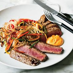 a white plate topped with meat and veggies next to a knife and fork