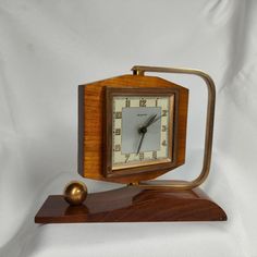 a small wooden clock on a stand with a ball in front of it and a white background