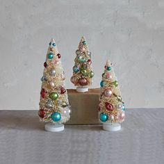 three small christmas trees with pearls and beads on them, sitting on a wooden block