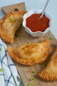 three pastries on a cutting board with dipping sauce