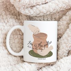 a coffee mug with the words, he is the potter on it sitting on a blanket