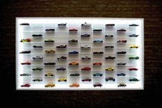 there are many toy cars on display in the wall with lights above them and below it is a white shelf that holds several different types of toys