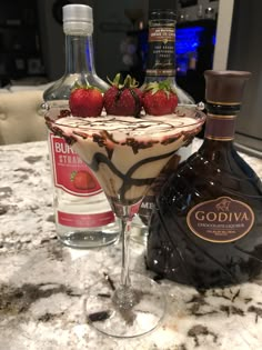 a chocolate martini with strawberries on the rim next to a bottle of booze