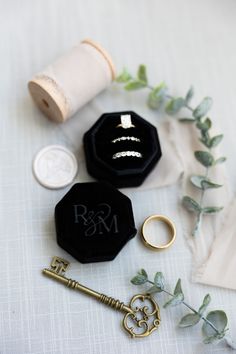 wedding rings, ring box and key laying on table next to spool of thread