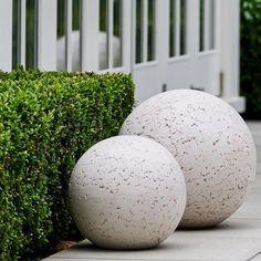 two white balls sitting next to each other on top of a cement slab near bushes