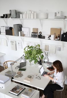 a woman sitting at a desk with a laptop computer and plant in front of her