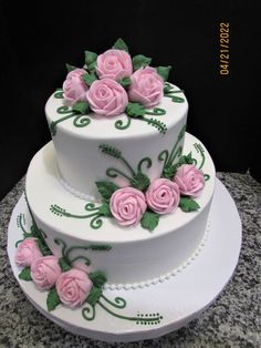 a three tiered cake with pink roses on the top and green leaves on the bottom